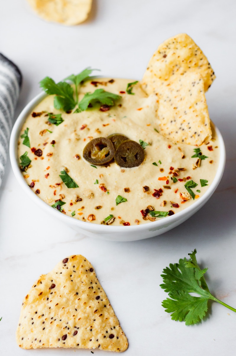 vegan queso in a white bowl topped with cilantro, jalapeños and chili flakes