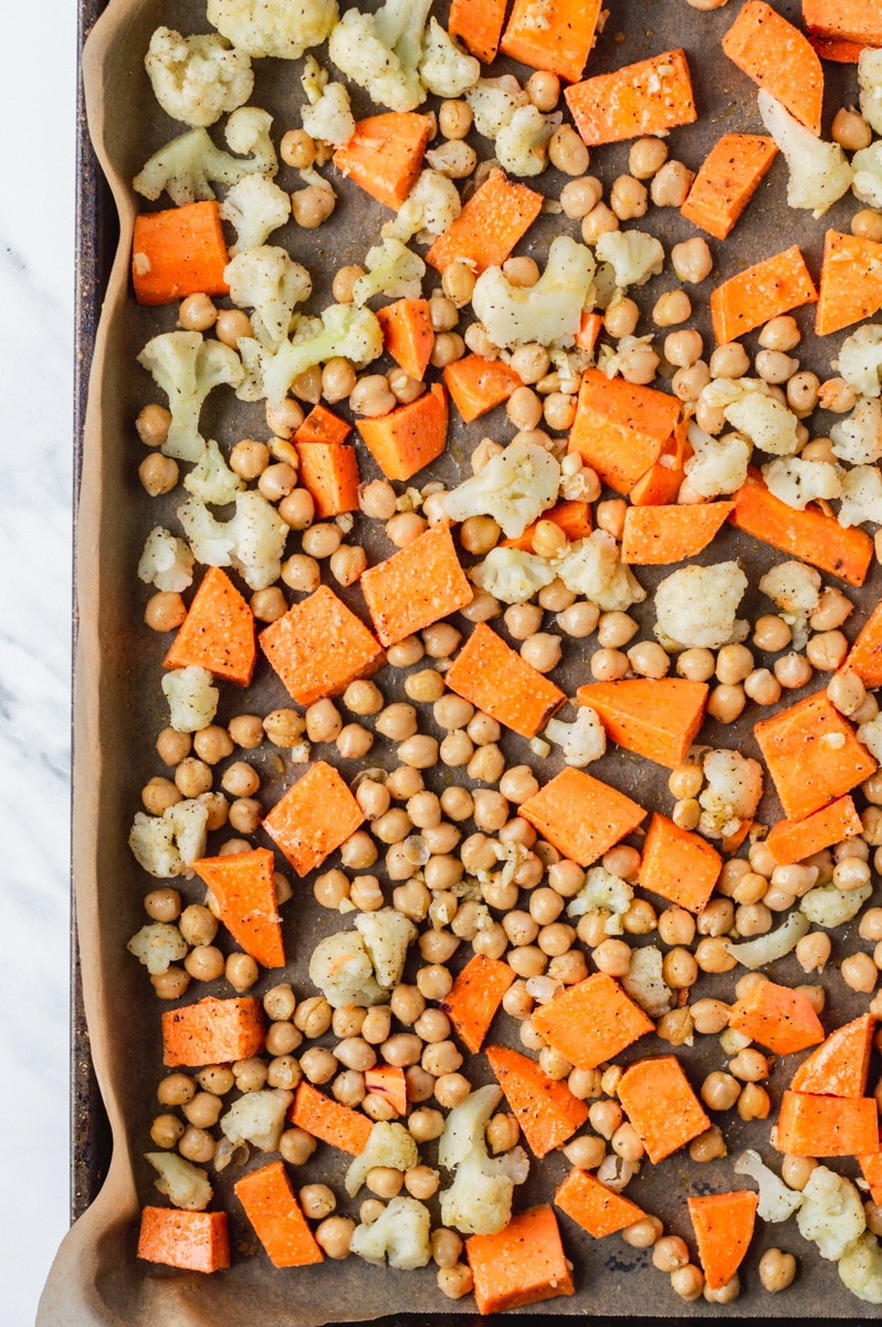 seasoned chickpeas, sweet potatoes and cauliflower florets on a baking sheet