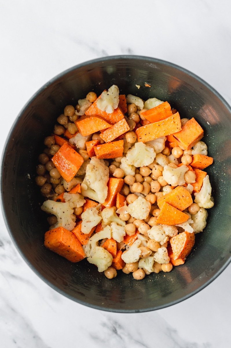 cauliflower, chickpeas and sweet potatoes tossed with oil in a bowl