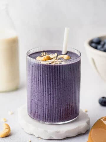vegan blueberry banana smoothie in a ribbed glass with cashew butter and blueberries