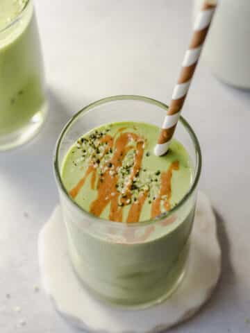 a peanut butter green protein smoothie in a glass with a brown and white straw