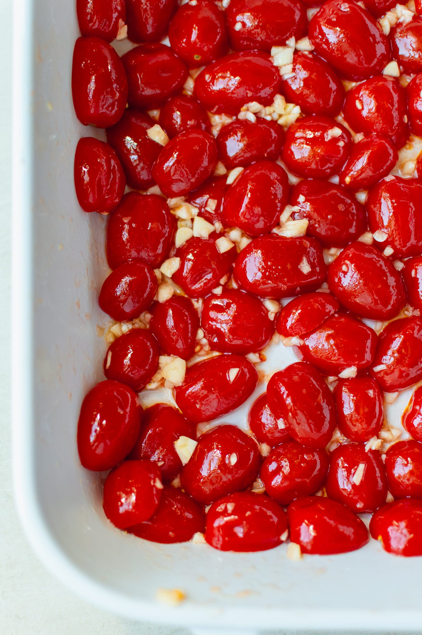 Halved grape tomatoes with garlic and olive oil arranged in a baking dish before roasting
