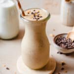 Chunky monkey smoothie in a glass topped with cacao nibs and peanuts, with ingredients in the background