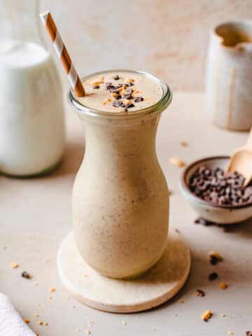Chunky monkey smoothie in a glass topped with cacao nibs and peanuts, with ingredients in the background