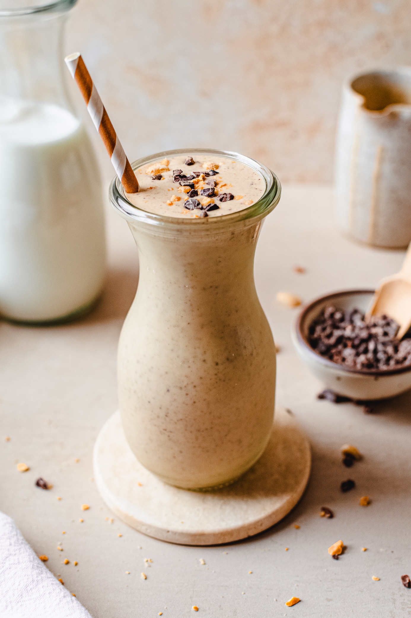 Chunky monkey smoothie in a glass topped with cacao nibs and peanuts, with ingredients in the background
