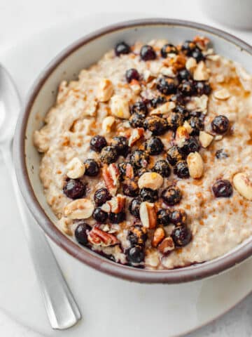 Creamy peanut butter oatmeal topped with blueberries, cinnamon, chopped peanuts and pecans