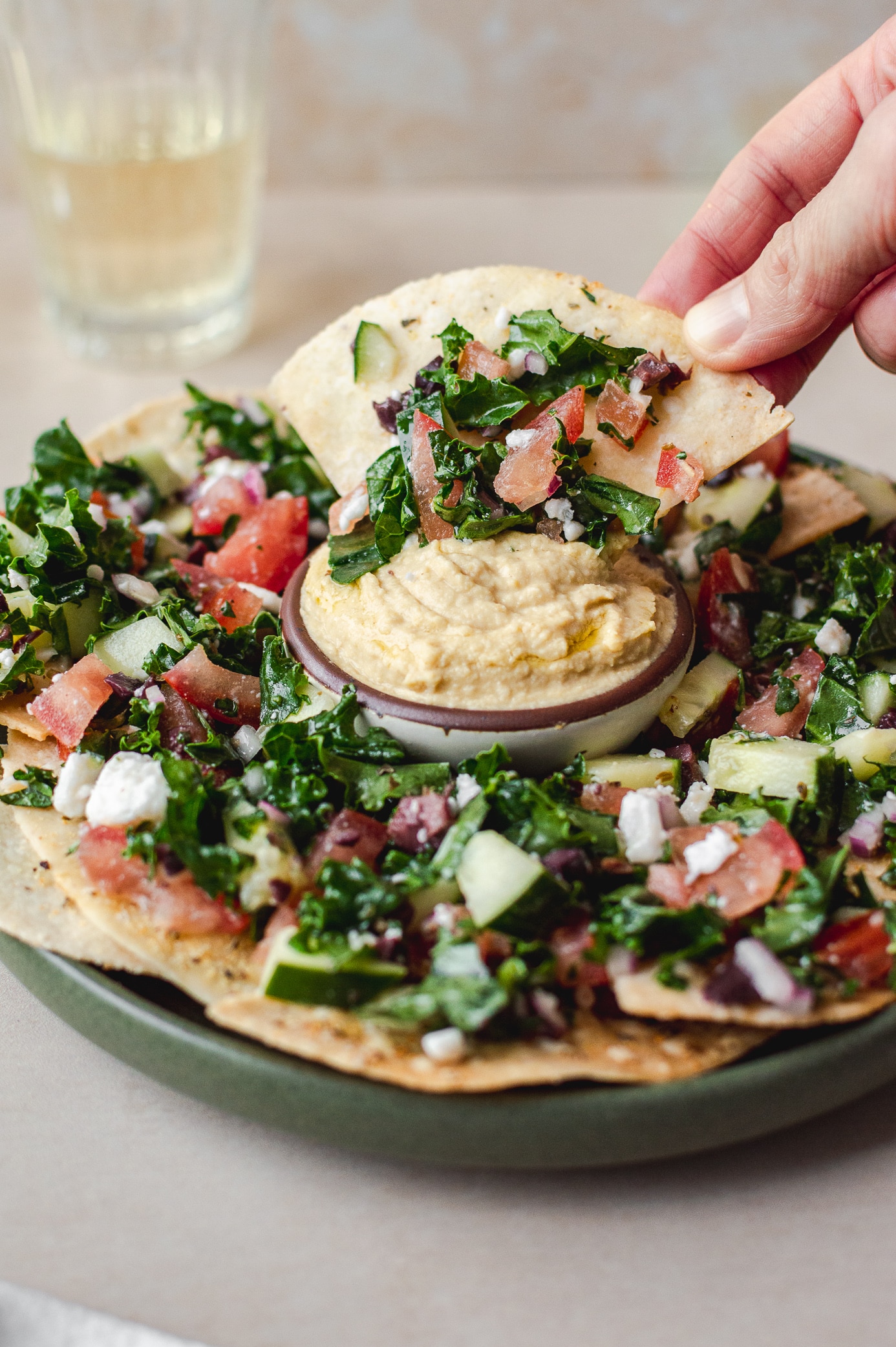 Scooping vegan Mediterranean nachos into hummus with a gluten-free pita chip