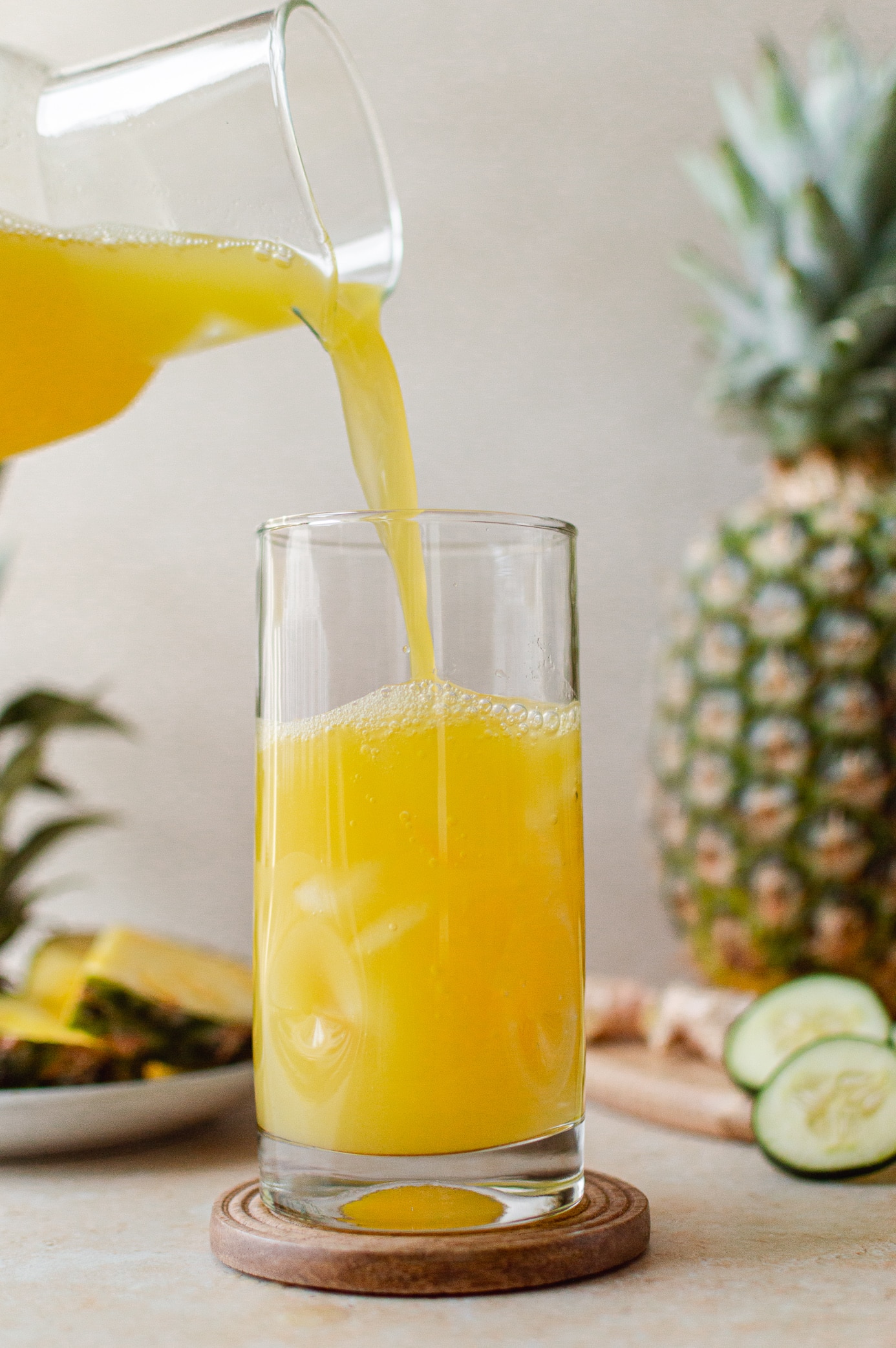 Pouring fresh pineapple cucumber juice into a glass filled with ice