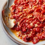 Roasted cherry tomatoes with garlic in a baking dish with a serving spoon