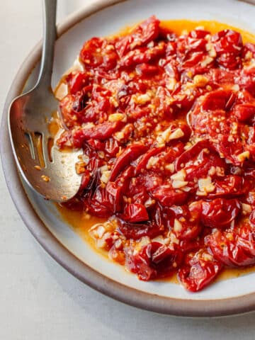 Roasted cherry tomatoes with garlic in a baking dish with a serving spoon