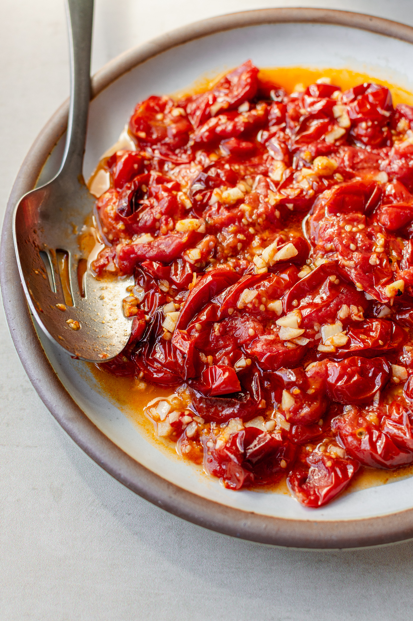 Roasted cherry tomatoes with garlic in a baking dish with a serving spoon