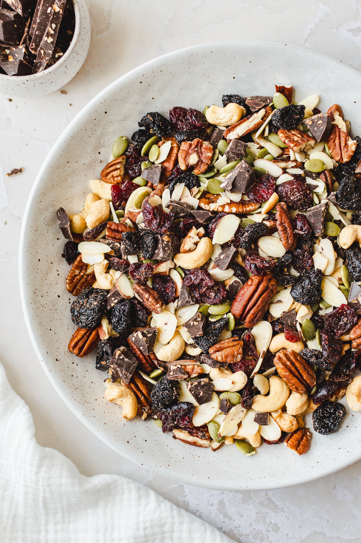 Homemade vegan trail mix with dark chocolate chunks in a speckled ceramic bowl.