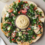 Vegan Mediterranean nachos with gluten-free pita chips, hummus, kale salad, olives, and vegan feta served with wine