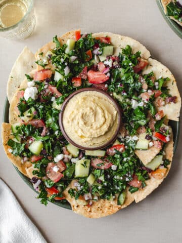 Vegan Mediterranean nachos with gluten-free pita chips, hummus, kale salad, olives, and vegan feta served with wine