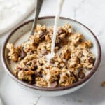 Chocolate chip cookie dough granola clusters in a ceramic bowl with milk being poured over the top.