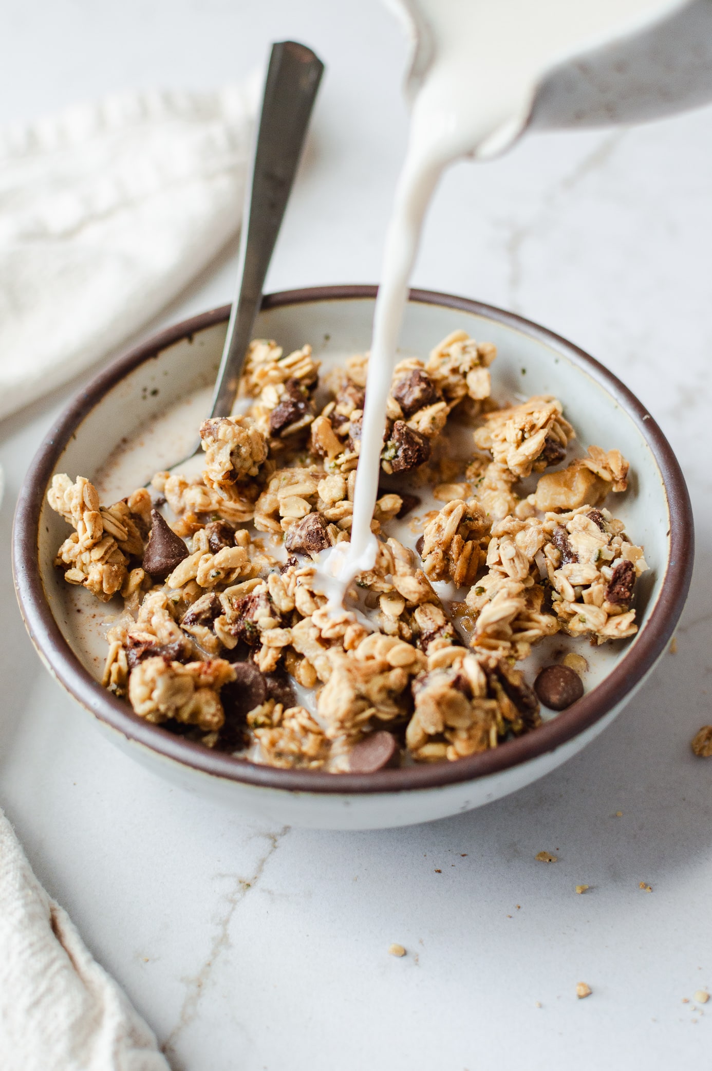 Chocolate chip cookie dough granola clusters in a ceramic bowl with milk being poured over the top.