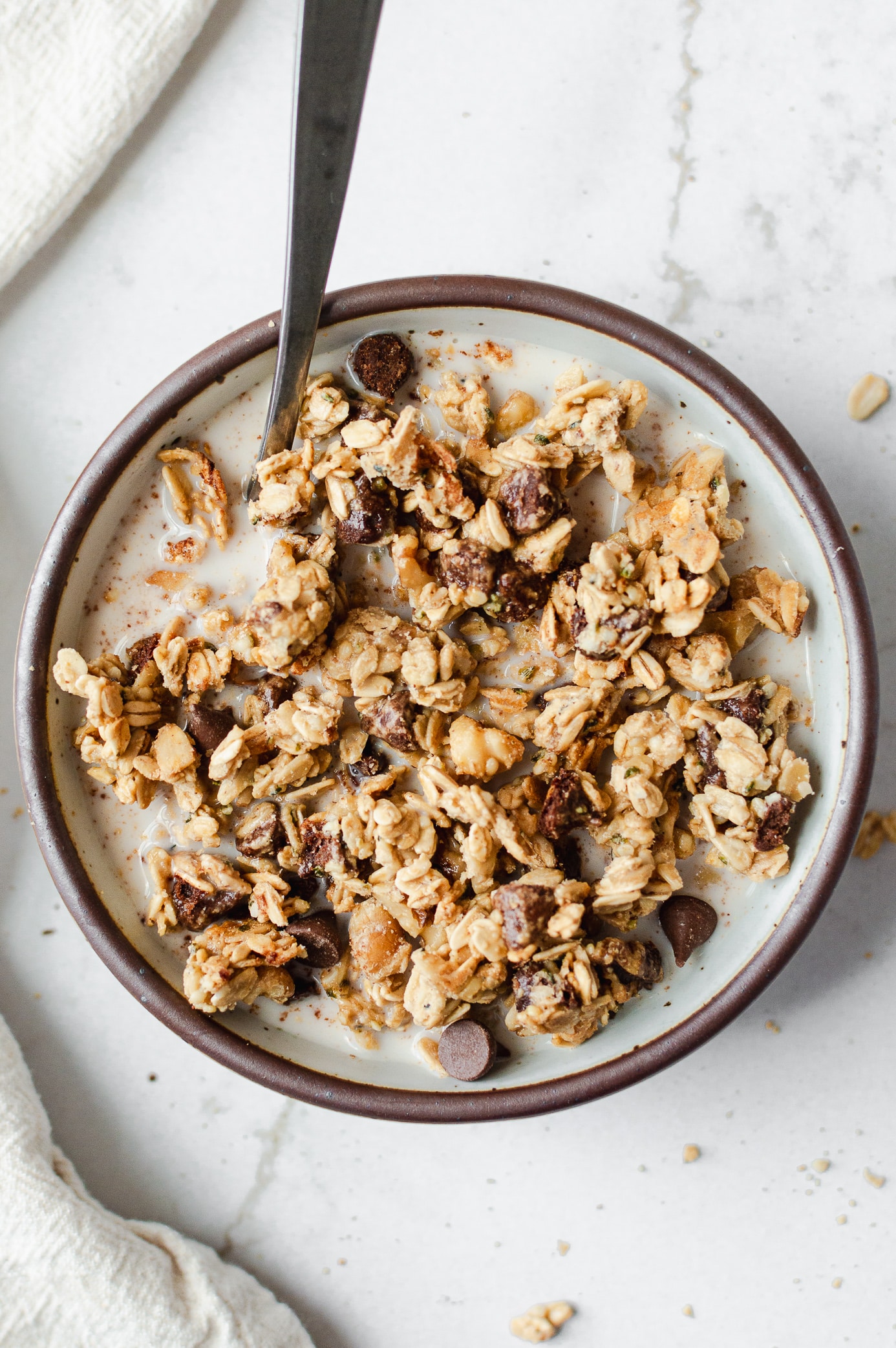 Chocolate chip cookie granola clusters in a bowl with milk, chocolate, walnuts, and hemp seeds