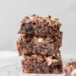 Stacked fudgy zucchini brownies topped with chopped pecans and melted chocolate chunks.