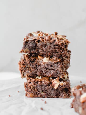 Stacked fudgy zucchini brownies topped with chopped pecans and melted chocolate chunks.