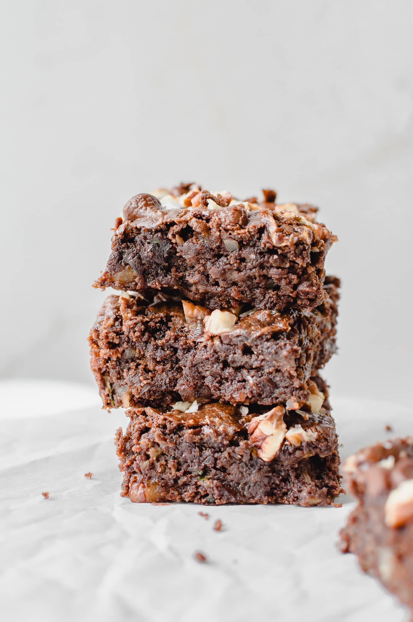 Stacked fudgy zucchini brownies topped with chopped pecans and melted chocolate chunks.
