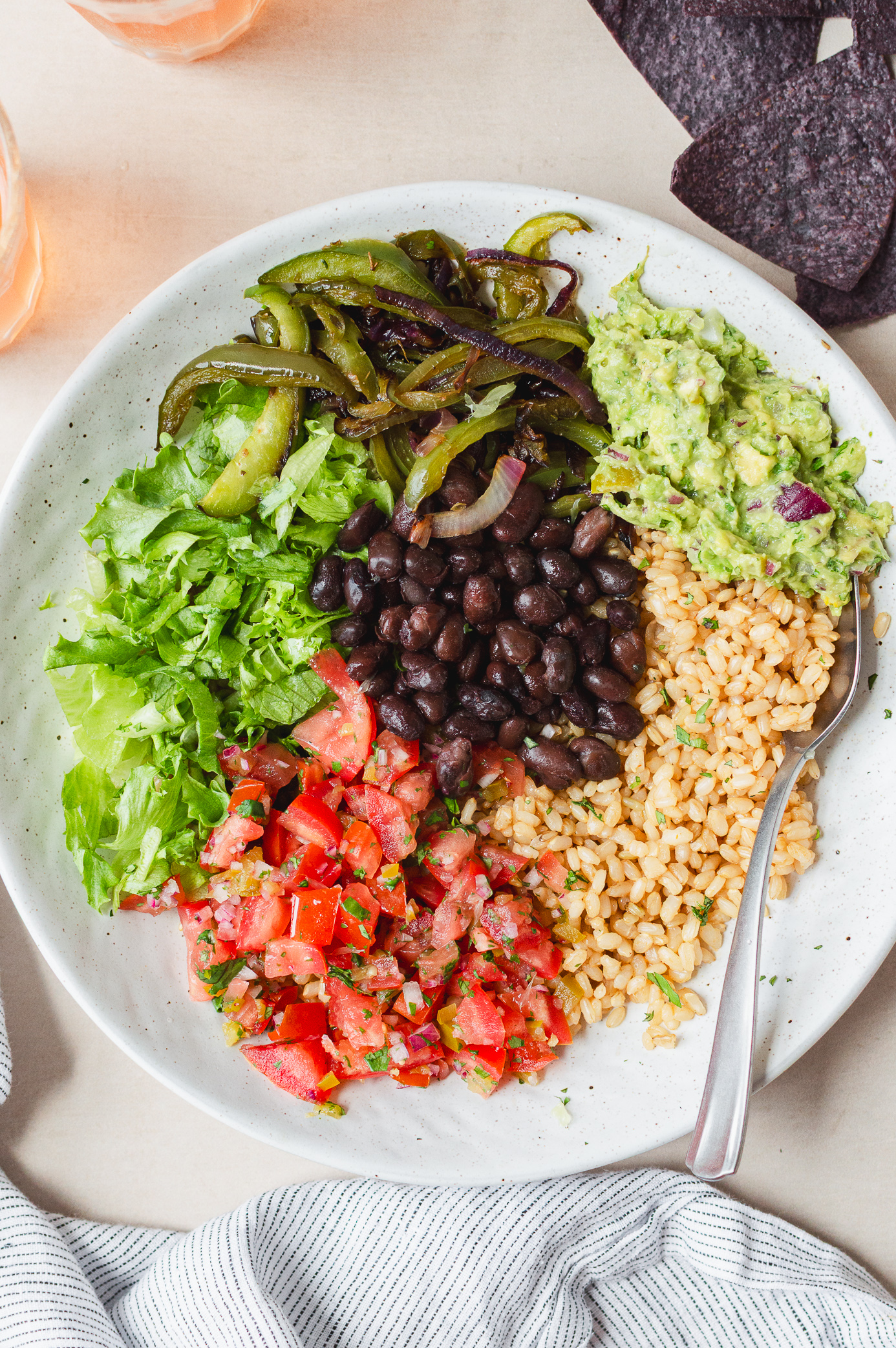 overhead shot of a veggie burrito bowl with beans, grilled veggies, guac, and salsa