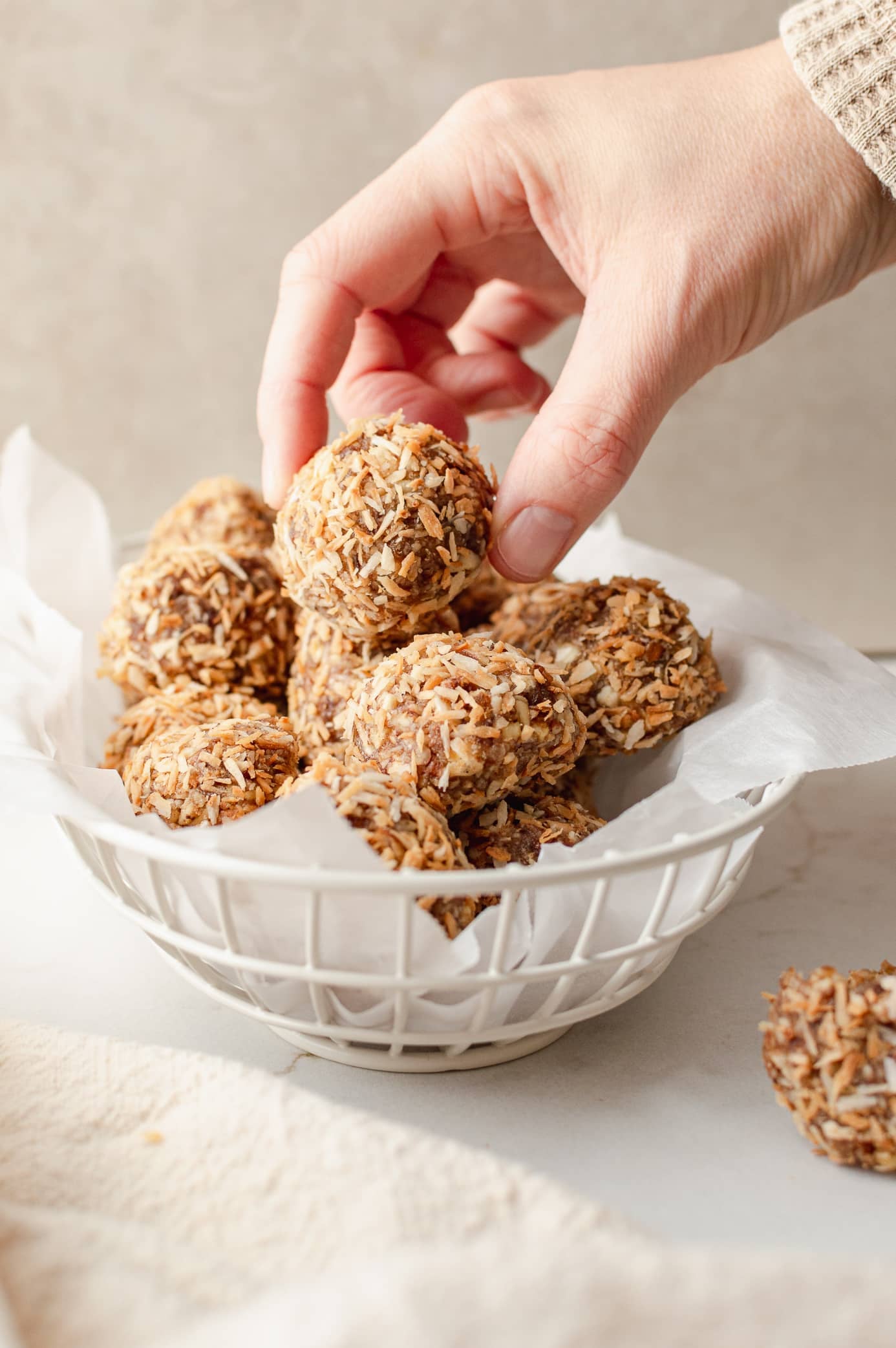 Hand taking a cinnamon coconut date bite from a basket of toasted coconut-coated bites