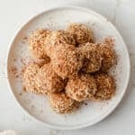 cinnamon coconut date bites on a plate topped with toasted coconut and cinnamon
