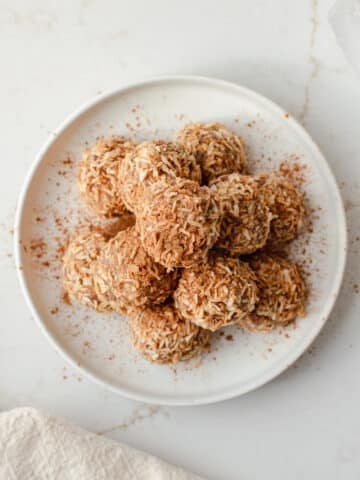 cinnamon coconut date bites on a plate topped with toasted coconut and cinnamon