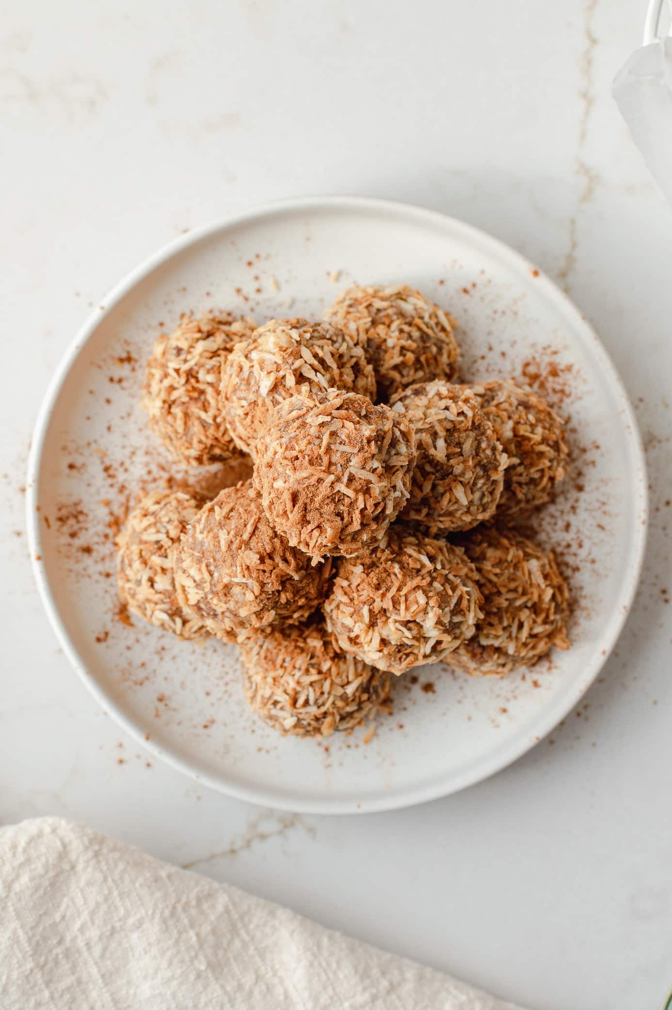 cinnamon coconut date bites on a plate topped with toasted coconut and cinnamon